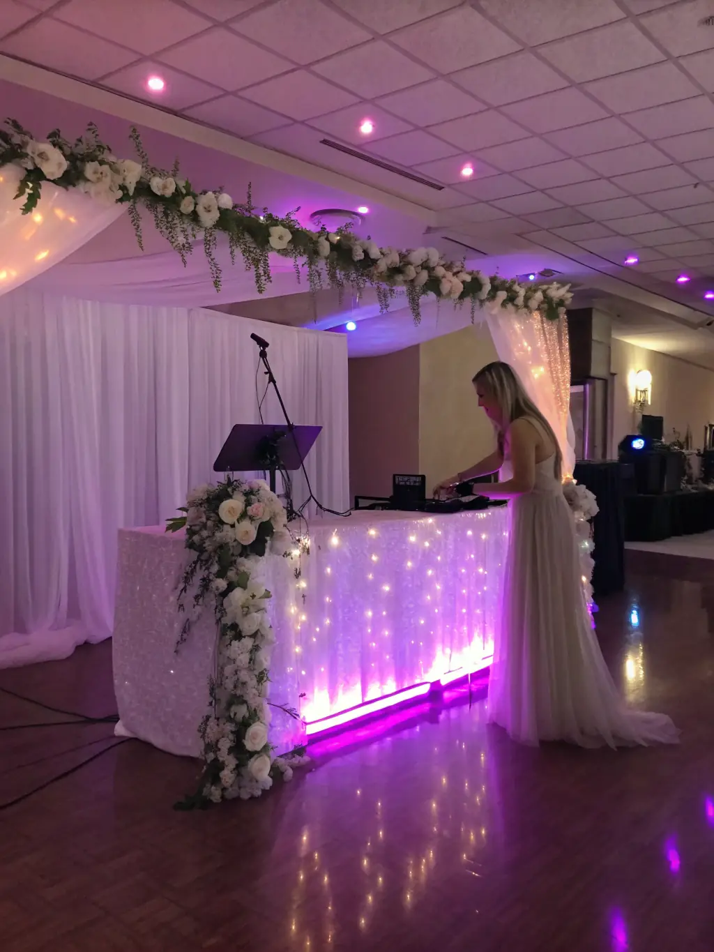 A beautifully decorated wedding reception with a DJ booth set up, ready for the evening's entertainment. The lighting is soft and romantic, creating a magical atmosphere.